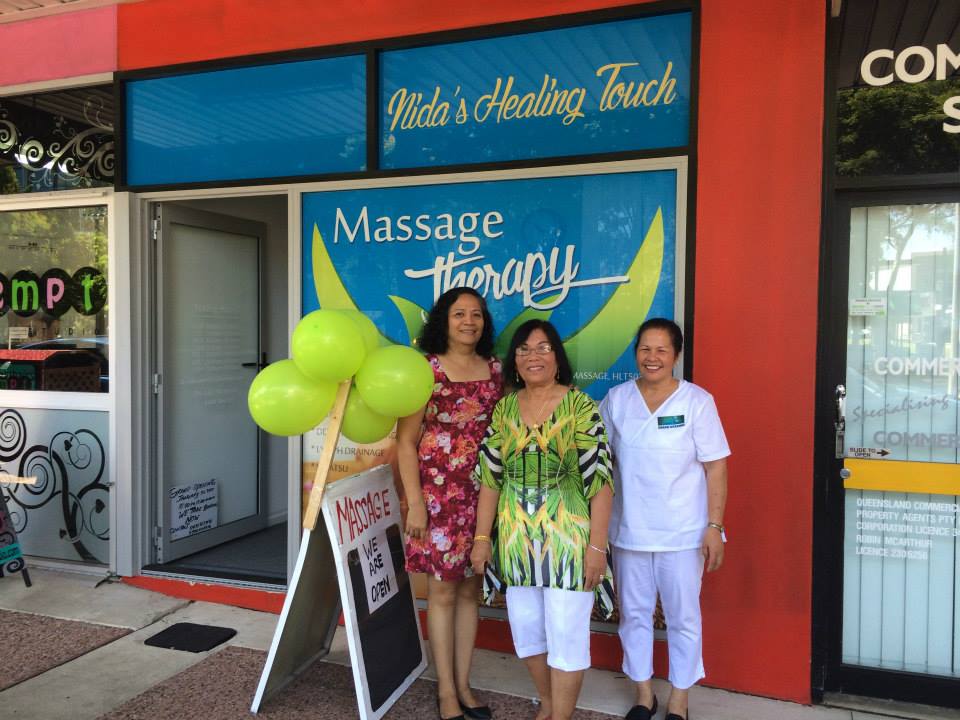 Three women outside the Nida's Healing Touch Massage Therapy shopfront on King Street on opening day, with balloons and a We Are Open sign