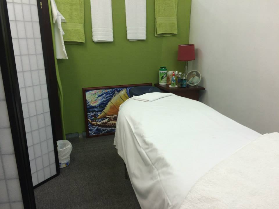 Treatment room with a freshly made massage table and green feature wall hung with towels