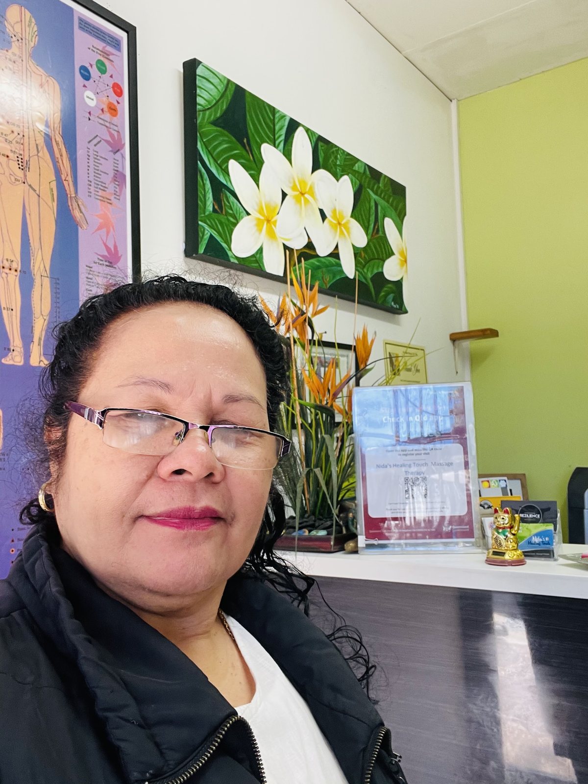 Nida at the front of her clinic, with frangipani artwork and reception behind her