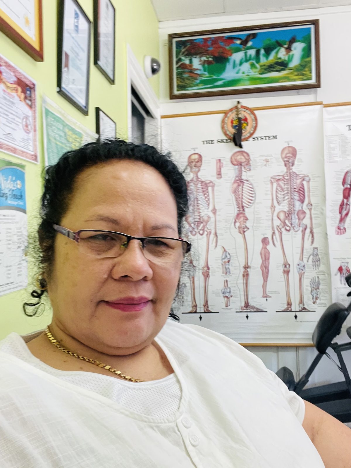 Nida in her treatment room, with an anatomy chart and her framed certificates on the wall behind her